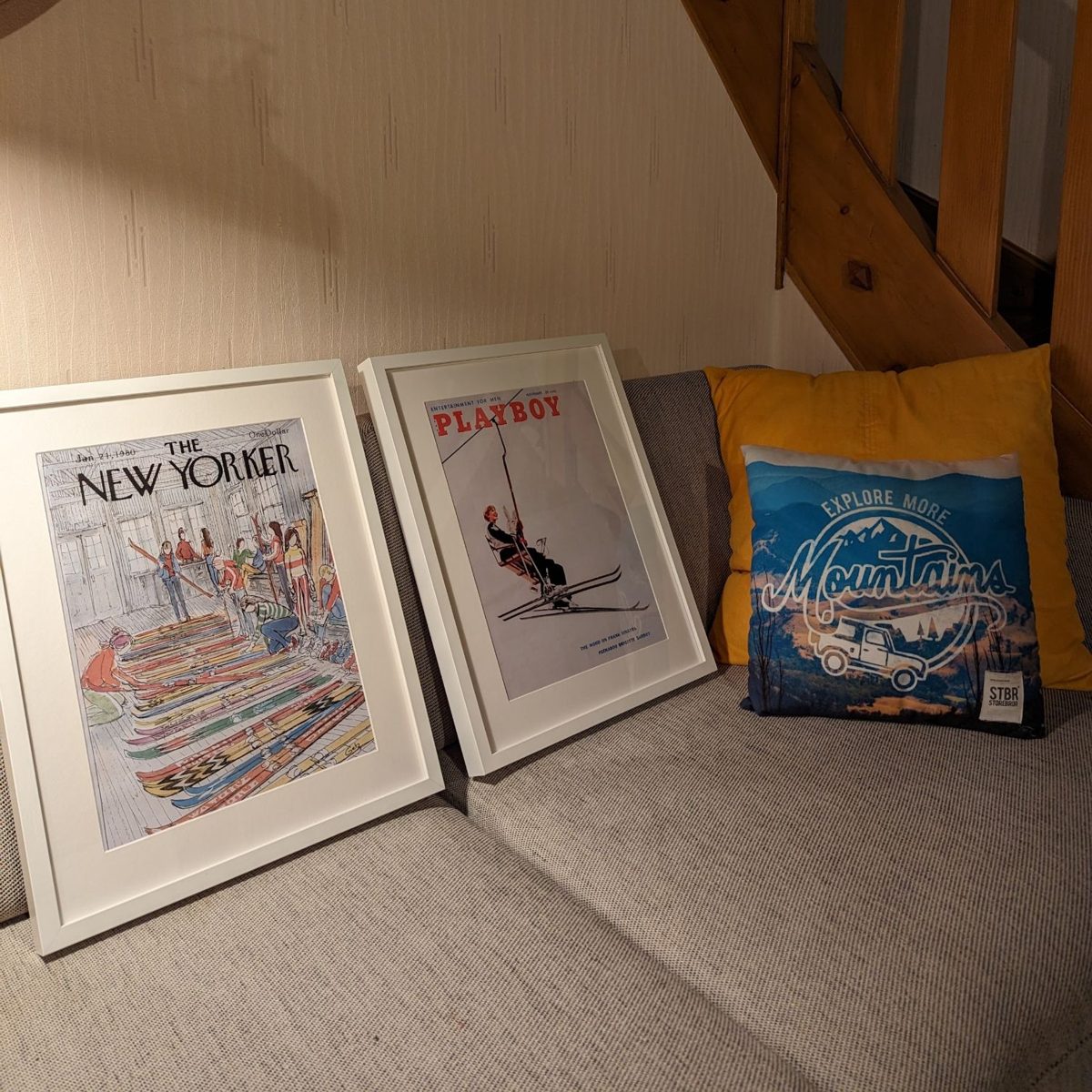 Framed New Yorker and Playboy ski covers on the sofa beneath the chalet staircase